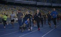Group of people running on tracks of the stadium, woman running and pushing the wheelchair with disabled boy, cerebral palsy