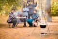 Group of people sitting at tourist table and eating food. People in casual wear rest in forest