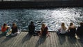 A group of people sitting on the waterfront in Copenhagen and looks out at the passing swimmers