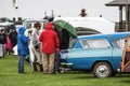 Group of people stand in raincoats with an umbrella talking in the rain at a classic car show