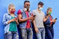 Group of people using their smartphones in covid 19 times protected with face mask - Friends checking online news while standing Royalty Free Stock Photo