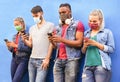 Group of people using their smartphones in covid 19 times protected with face mask - Friends checking online news while standing Royalty Free Stock Photo