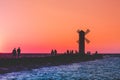 A group of people walk along the pier near the lighthouse on the sea at sunset Royalty Free Stock Photo