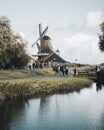 Group of people walking along a path toward a picturesque windmill on the bank of a river Royalty Free Stock Photo