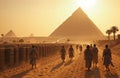 A group of people walking on a sandy road in front of the pyramids Royalty Free Stock Photo