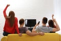 Group of people watching TV together on sofa in living room.