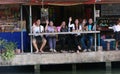 A group of people wave from the edge of the canal at Amphawa Floating Market