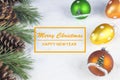 Group of pine trees, some branches and colorful baubles and Christmas balls with text in English `Merry Christmas, happy new year`