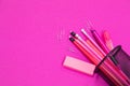 Group of pink color stationery products is spilled from pencil box on pink surface flatlay isolated