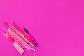 A group of pink office requisites is lying in the lower left corner on pink background isolated