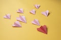 Group of pink paper aeroplane origami following the red one on yellow background