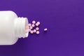 Group pink tablets. Capsules spilling out of white bottle. Purple background. Royalty Free Stock Photo