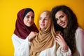 Group portrait of beautiful Muslim women two of them in a fashionable dress with hijab isolated on a yellow background Royalty Free Stock Photo