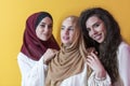 Group portrait of beautiful Muslim women two of them in a fashionable dress with hijab isolated on a yellow background Royalty Free Stock Photo