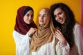 Group portrait of beautiful Muslim women two of them in a fashionable dress with hijab isolated on a yellow background Royalty Free Stock Photo