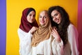 Group portrait of beautiful Muslim women two of them in a fashionable dress with hijab isolated on a yellow background Royalty Free Stock Photo