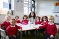 Group portrait of infant school teacher and kids sitting at table in a classroom looking to camera smiling, front view Royalty Free Stock Photo