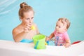 Group portrait of white Caucasian mother and baby daughter playing with toys in water on swimming poo nosing inside, training to