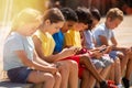 Positive children with mobile devices sitting at urban street