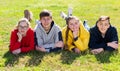 Group of positive teenagers lying on green grass