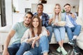 Group of positive young friends enjoying movie at home, eating popcorn, switching channels with remote control Royalty Free Stock Photo