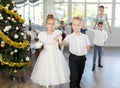 Group of preteen children in festive clothes dances waltz around Christmas tree Royalty Free Stock Photo