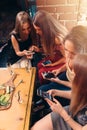 Group of pretty young female friends eating together in cafe using smartphones