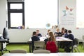 A group of primary school kids sitting at table in a classroom, teacher kneeling to help them during the lesson Royalty Free Stock Photo