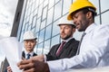 Group of professional architects in helmets working with blueprint outside modern building Royalty Free Stock Photo