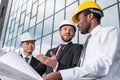 Group of professional architects in helmets working with blueprint outside modern building Royalty Free Stock Photo