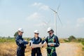 Group of professional technician man and woman workers discuss about work project on plan paper in front of wind turbine or Royalty Free Stock Photo