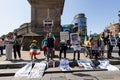 Group of protesters standing in a line in front of a large statue, holding up signs and banners