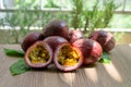 A group of purple skin passionfruit plant, sliced and round fruits under sunlight morning on wooden table, blurred background