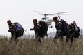 A group of rescuers walk along a burning field in fire-fighting uniforms amid a flying rescue helicopter.