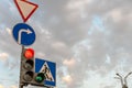 A group of road signs and a traffic light with an additional section at the intersection against the sky. A red traffic light and