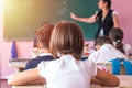 group of school kids sitting and listening to teacher in classroom from back