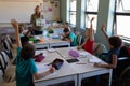 Group of schoolchildren raising their hands in an elementary school classroom