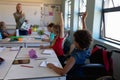 Group of schoolchildren sitting at desks raising their hands in an elementary school classroom