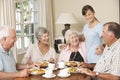 Group Of Senior Couples Enjoying Meal Together In Care Home With Teenage Helper