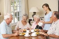 Group Of Senior Couples Enjoying Meal Together In Care Home With Teenage Helper