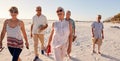 Group Of Senior Friends Walking Along Sandy Beach On Summer Group Vacation Royalty Free Stock Photo