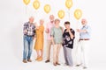 Senior people with yellow balloons standing in empty white room