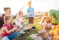 Group of six Kids: Boys and girls cheerfully smiling and roasting sausages on sticks over a campfire flame near the green tent. Royalty Free Stock Photo