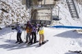 Group of skiers and snowboarders at a snow-covered mountain base, waiting beside a ski lift.