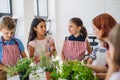 A group of small school kids with teacher standing in circle in class, planting herbs.