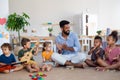Group of small nursery school children with man teacher sitting on floor indoors in classroom, playing musical Royalty Free Stock Photo