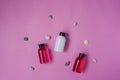 Group of small travel bottles for body care and sea pebbles on pink background