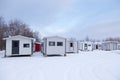 Group of small white ice fishing huts with black trim seen during an early winter morning