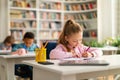 Group of smart school children sitting at desks in classroom or library at primary school, writing in their workbookk Royalty Free Stock Photo