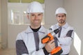 Group smiling builders in hardhats with electric drill indoors Royalty Free Stock Photo